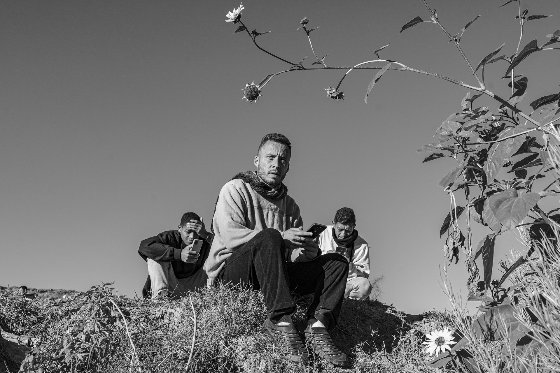 Venezuelan migrants using their phones just a few meters from the border, in Ciudad Juárez, Mexico. After the creation of a parole program by the US government, many are forced to wait for scarce asylum appointments in border cities controlled by corrupt authorities and drug cartels.