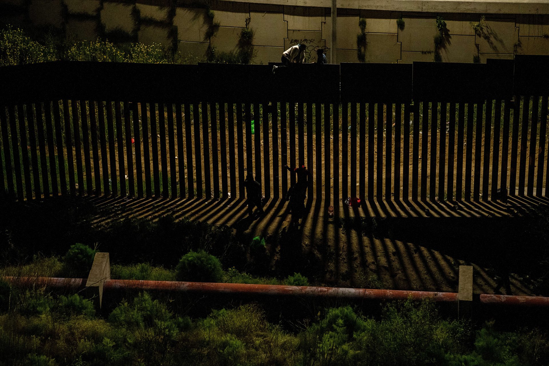 Migrants jump a border fence to enter the United States. In 2023, over 2.3 million people were apprehended at the southern border of the United States, where they face an uncertain future. Tijuana, Mexico.