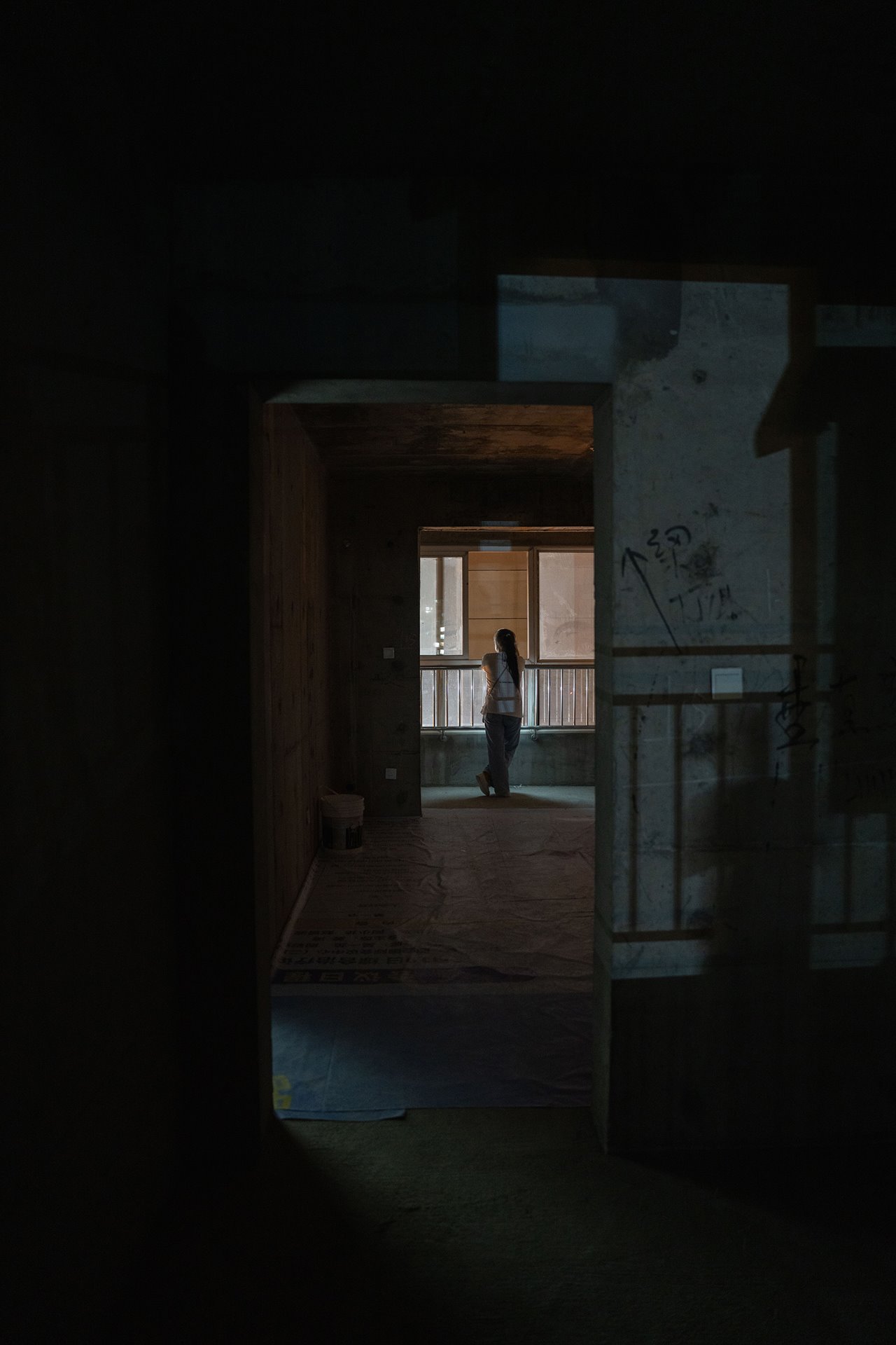 A homeowner looks out of a window in the Yihefang complex, Xi&rsquo;an, China. Approximately 200 families live in the unfinished apartment complex.