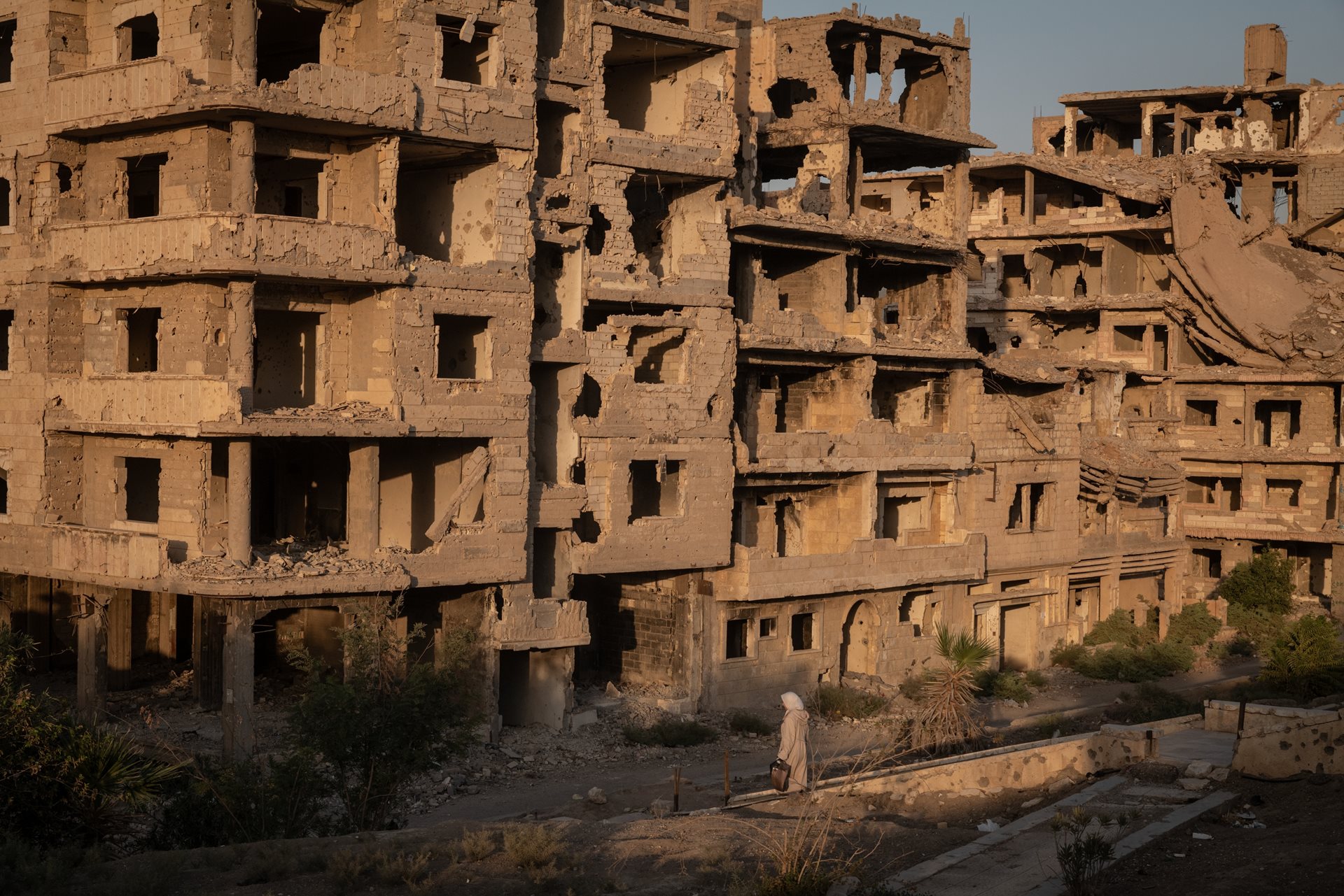 A woman walks through a damaged neighborhood in&nbsp;Deir al-Zour, Syria. Seventeen of the city&rsquo;s 25 neighborhoods were almost completely destroyed.