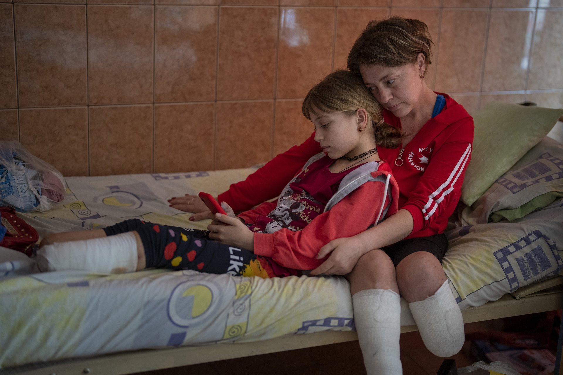 Natasha Stepanenko (43) sits on her bed with her daughter Yana (11) &nbsp;at a public hospital in Lviv, Ukraine. Natasha, together with Yana and her twin brother Yarik, were injured during shelling of a train station in the eastern city of Kramatorsk, on 8 April. According to the UN Human Rights Office, some 60 civilians were killed, and 110 wounded in a Russian missile strike on the station. Thousands of civilians were gathered there, awaiting evacuation. Russia denied involvement, claiming the strike was orchestrated by Ukraine. The family were later flown to San Diego, in the United States, where Yana and Natasha received new prostheses, and Yana underwent surgery.