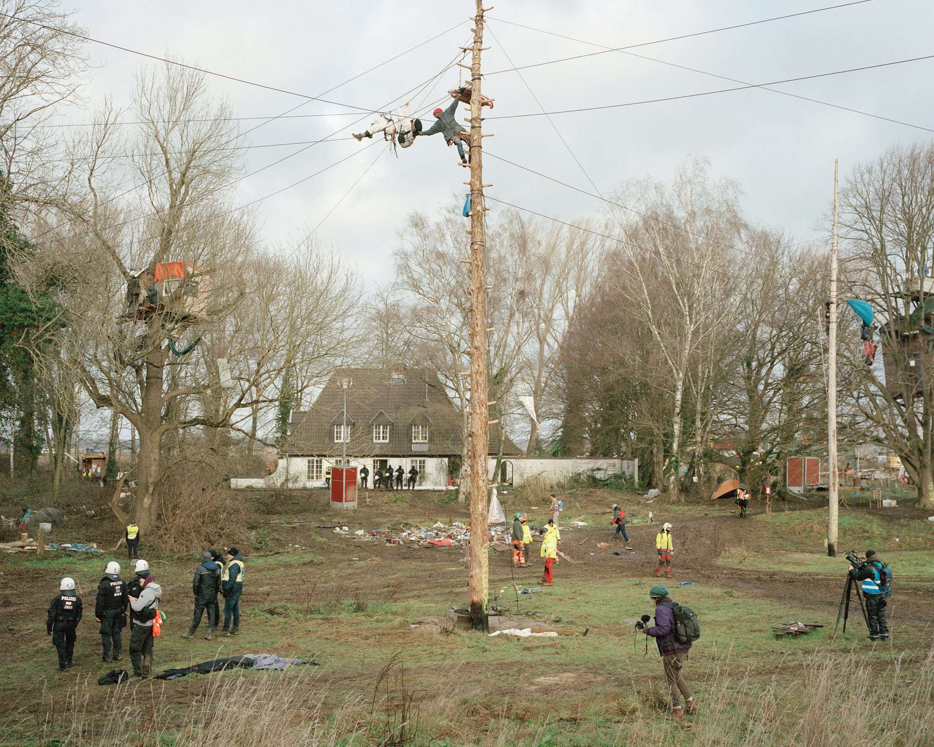 An activist on an access tower aids another, who is climbing along ropes from a treehouse, in Lützerath, Germany. These ropes sometimes allow activists to evade the police, who approach them on cherry pickers.