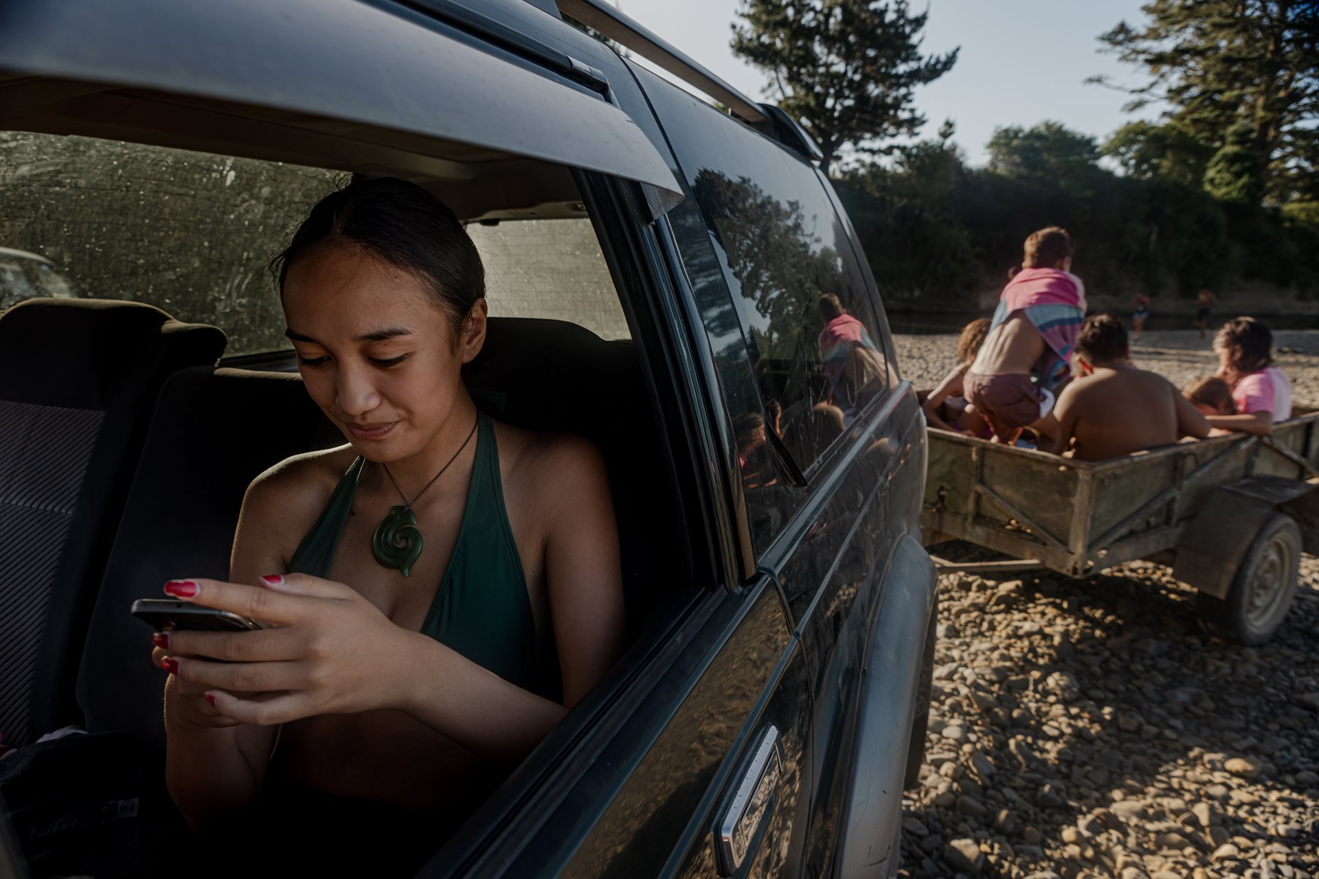 Te Paia Te Tana (16) catches up on messages after a daily swim in the Ōhinemataroa (Whakatane) River, in Ruatoki, New Zealand, before her cousin drives everyone back to the Teepa homestead.