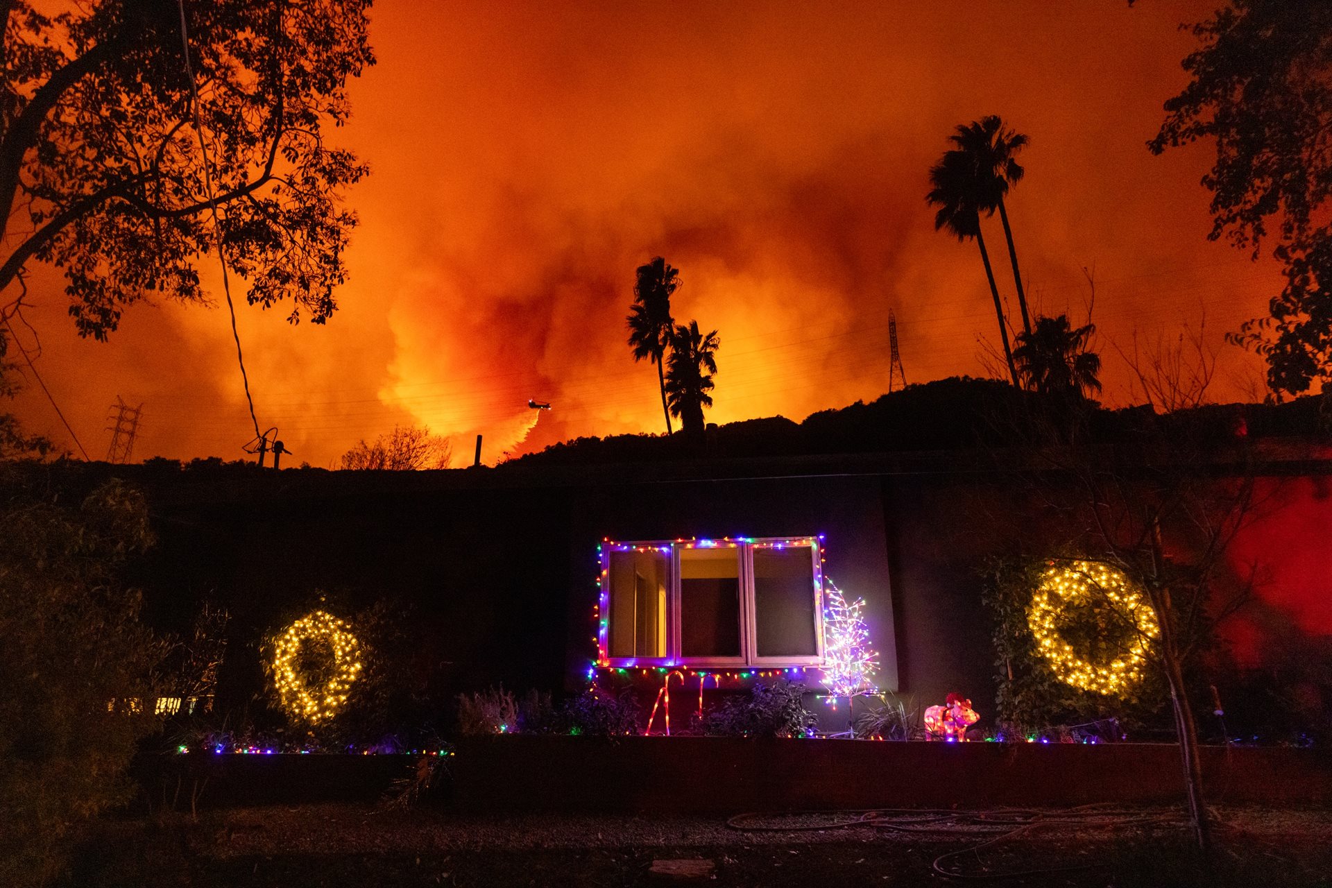 <p>A helicopter drops water behind a Mandeville Canyon home still decorated with Christmas lights. Firefighting efforts were severely hindered by the extreme Santa Ana winds driving the blazes. Los Angeles, California, United States</p>
