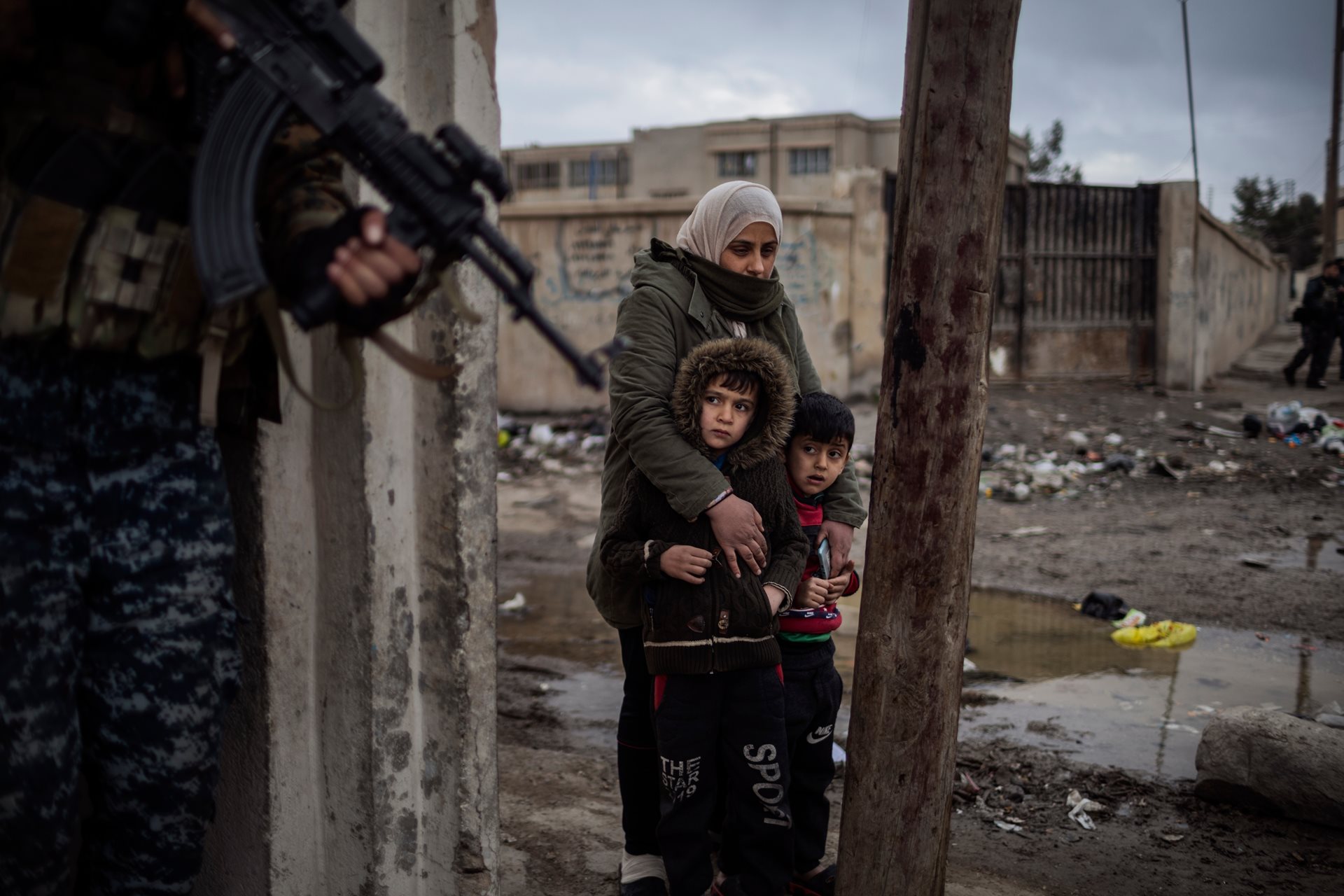 Nasreen holds her sons Mohamed and Saad outside their home in Al-Hasakah, Syria, while Kurdish special forces search inside for escaped prisoners and ISIS fighters.
