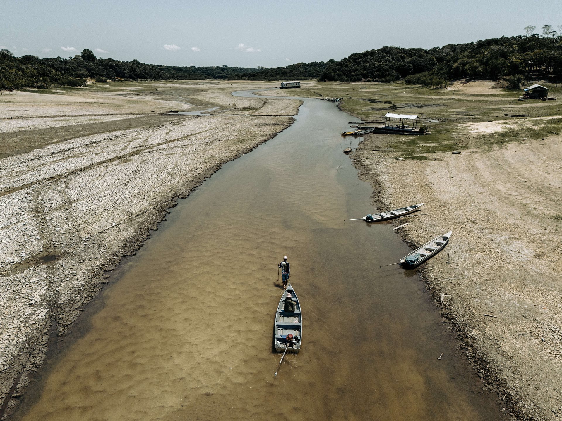 A man drags a boat through shallow water near São Francisco de Marina. Drought has grounded floating homes and made travel by river nearly impossible. Manaus, Amazonas, Brazil.