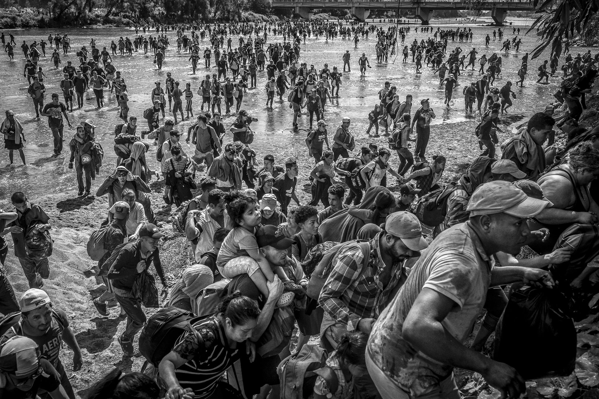 Ever Sosa carries his daughter on his shoulders as they cross the Suchiate River from Guatemala to Mexico, joining a caravan of 3,000 migrants and asylum seekers attempting to get to the United States. In 2019, Mexico granted humanitarian visas for a similar caravan, but by 2020, the policy shifted, calling for the dismantling of any caravan. Thus, thousands were forced to reach Mexico by crossing the Suchiate river rather than using the Dr. Rodolfo Robles International Bridge. Ciudad Hidalgo, Mexico.