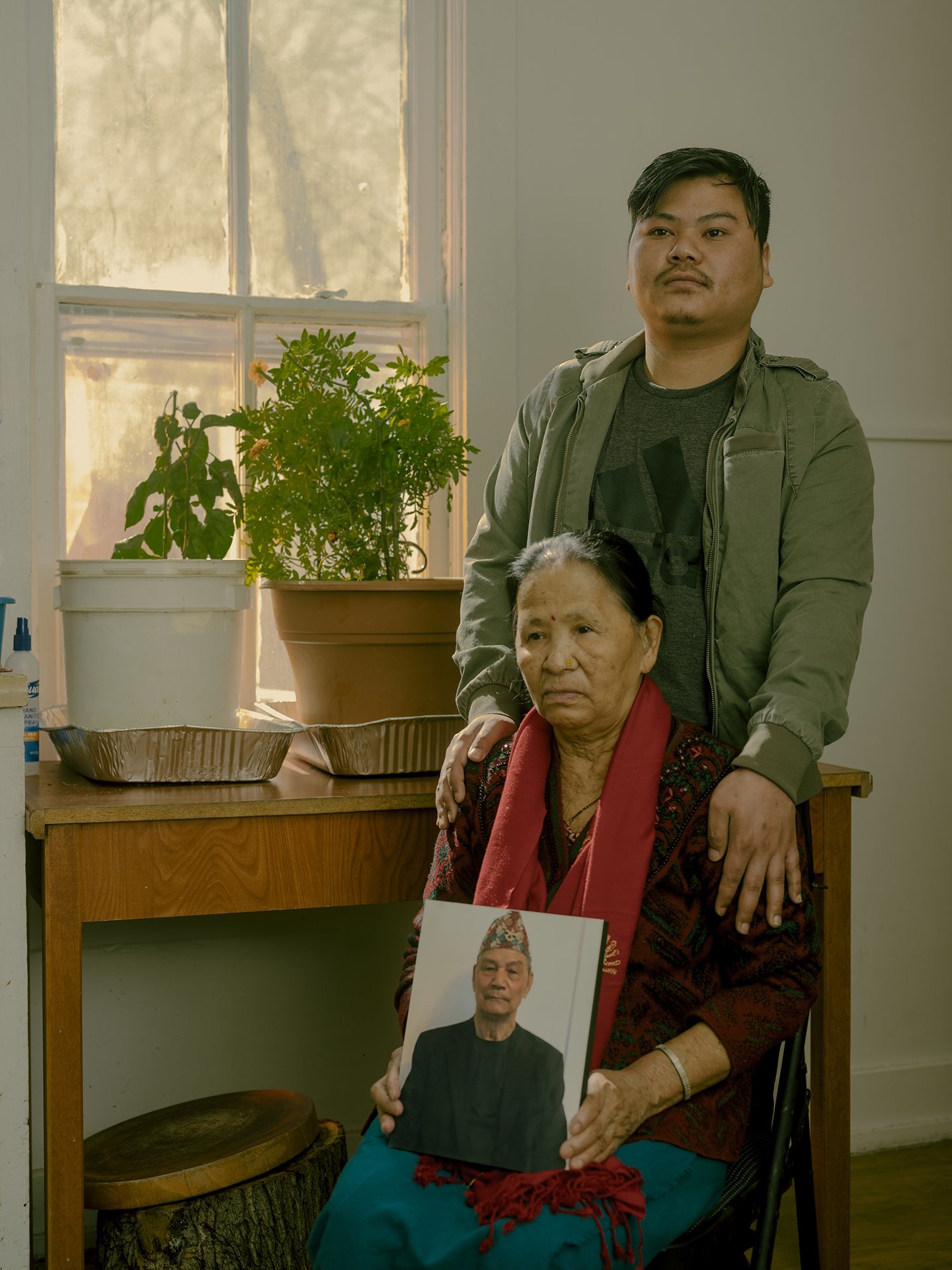 Man B. Ghale, poses with his mother and a portrait of his father, in Omaha, Nebraska, USA. Ghale came to Omaha from a Nepali refugee camp in 2013, and worked at a meatpacking plant. He suspects that he caught the coronavirus in cramped working conditions, and brought it home. His 75-year-old father died from COVID-19 complications in June 2020, and his mother was also ill with the disease.&nbsp;