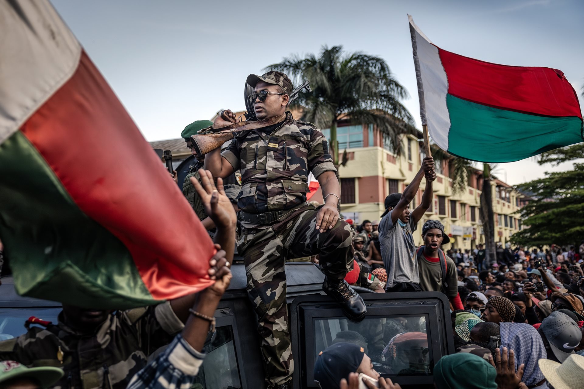 Protesters cheer and wave flags outside City Hall in Antananarivo, Madagascar as members of the CAPSAT military unit ride on an armored vehicle.