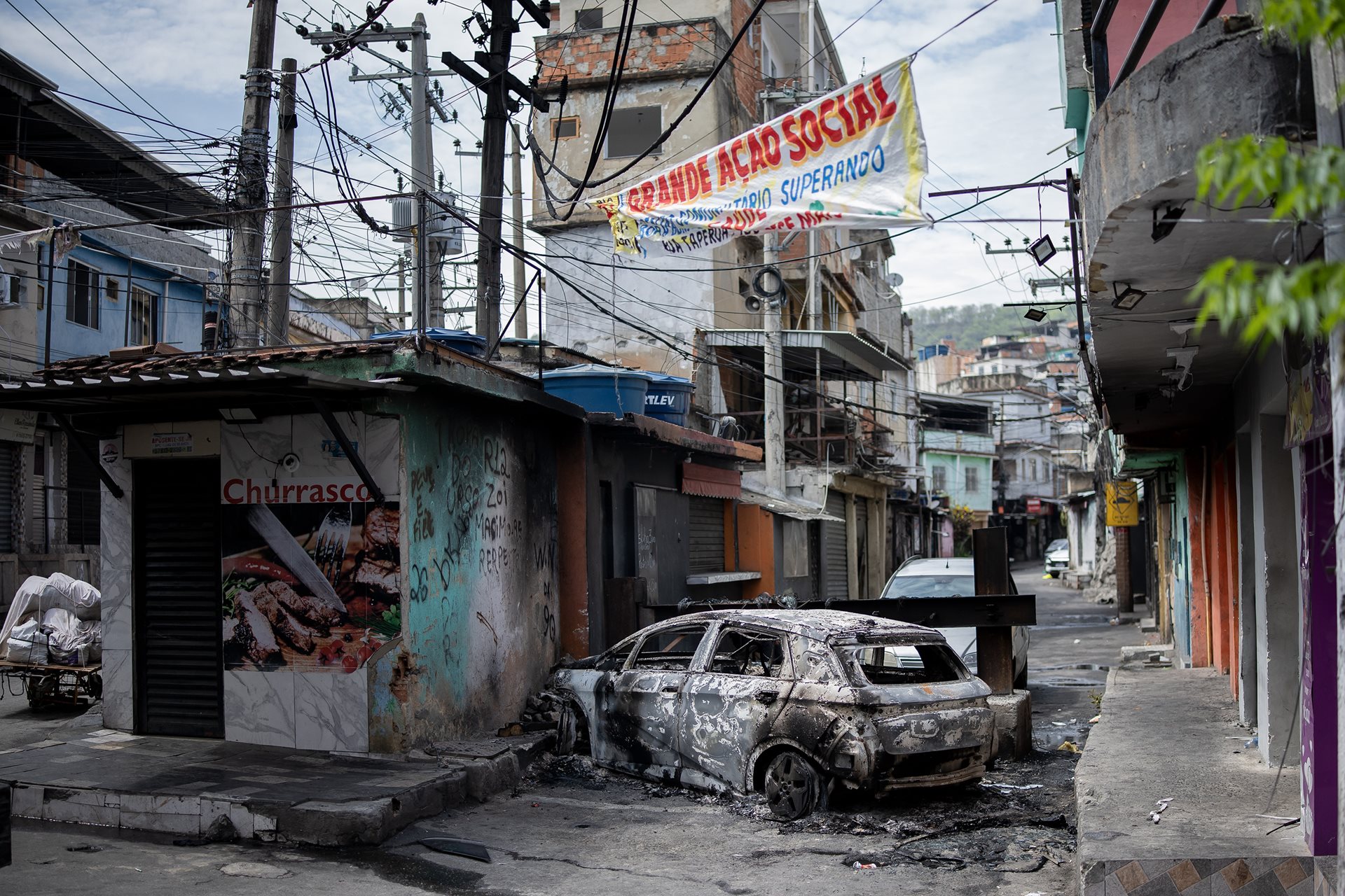 A vehicle burned by drug traffickers smolders at a barricade, hindering police access to the Penha complex in Rio de Janeiro, Brazil. Setting vehicles ablaze is a common tactic to delay advancing law enforcement.&nbsp;