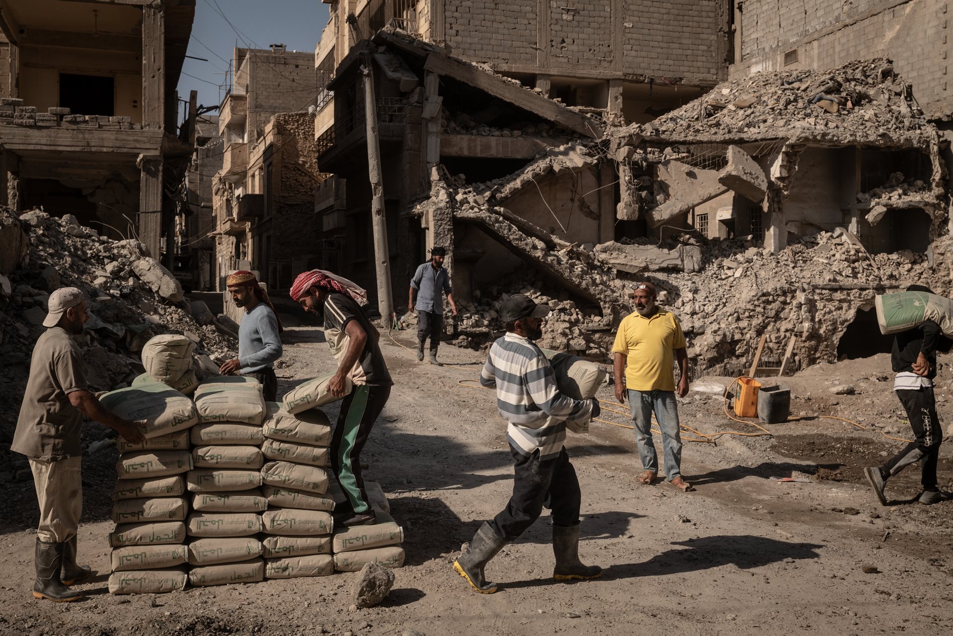 Day laborers prepare cement for mixing at a construction site next to destroyed buildings in&nbsp;in Deir al-Zour, Syria.