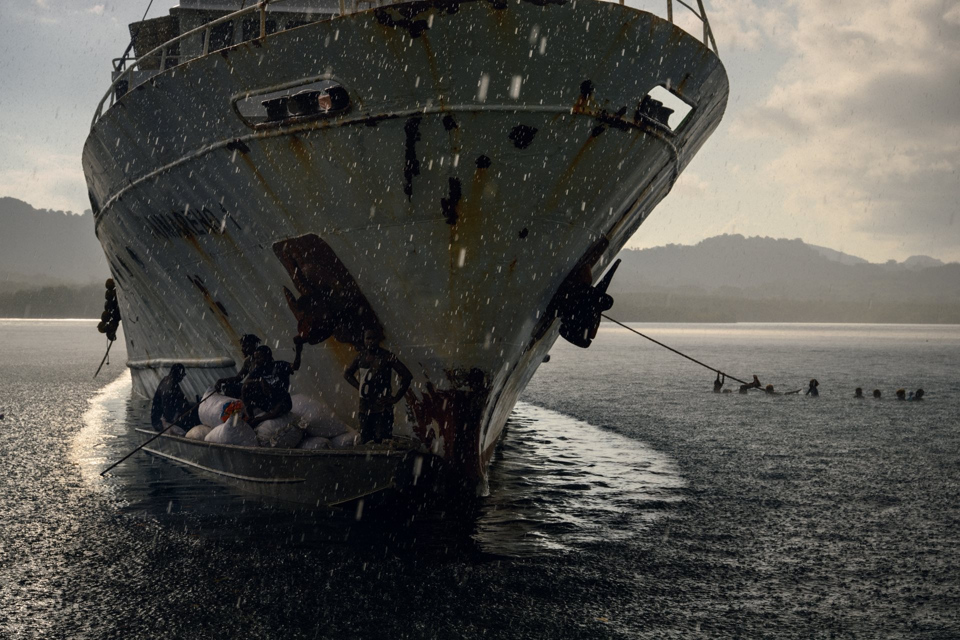 A boat shelters beneath a supply vessel, protecting bags of dried seaweed from a storm. This new export links the remote island to global markets. Fanalei Island, South Malaita, Solomon Islands.