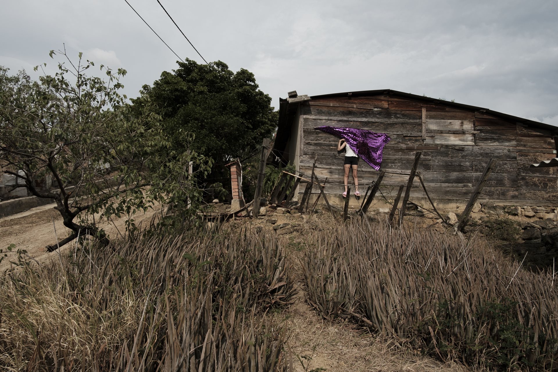 Gabriela (12) hides behind a cloth at her grandmother&rsquo;s house in Los Patios, Norte de Santander, Colombia. The house was built by her grandfather and uncle, who died in 2016 and 2023 respectively.