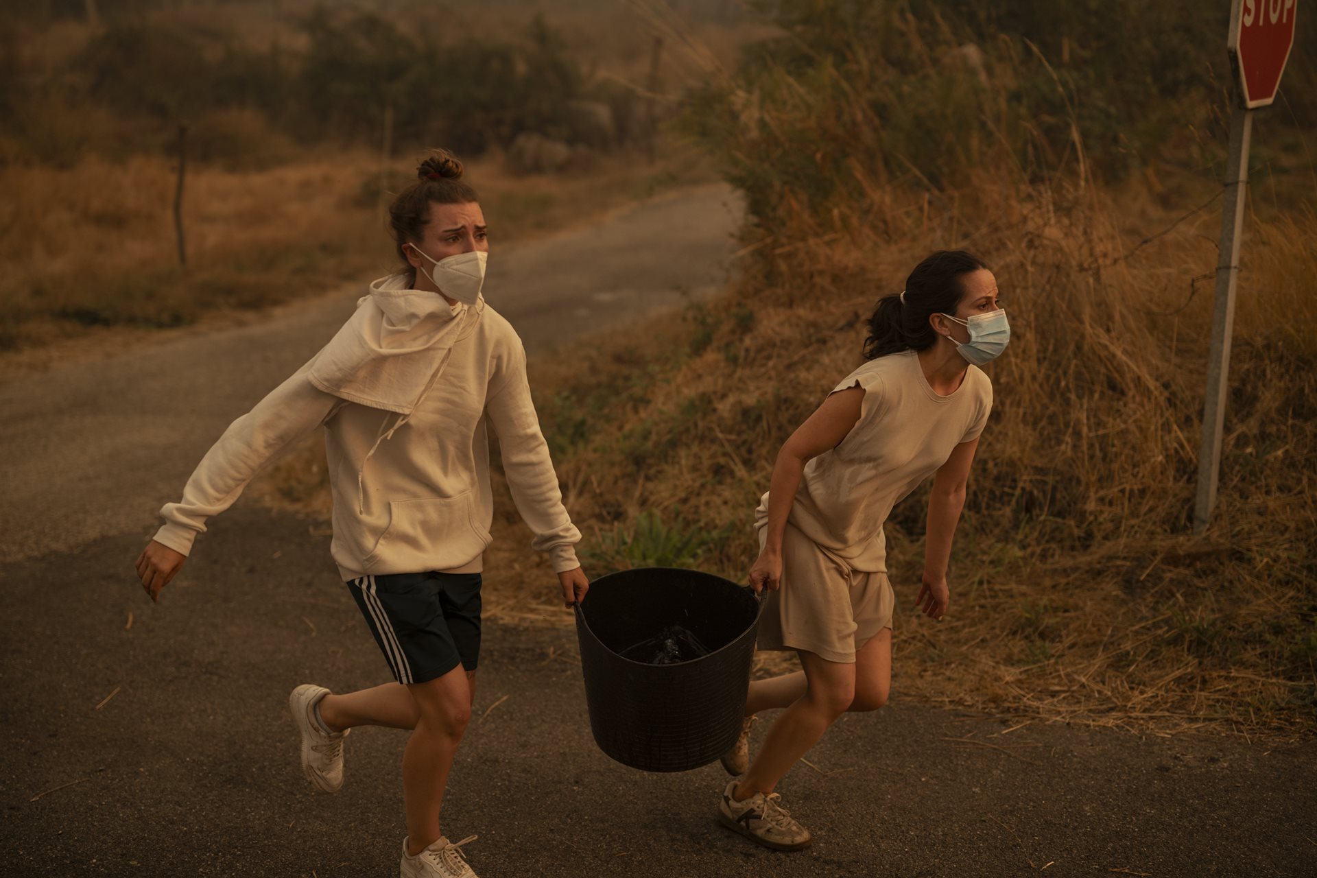 Two women run with a bucket of water to help fight a wildfire in Carballeda de Avia, Ourense, Galicia, Spain.