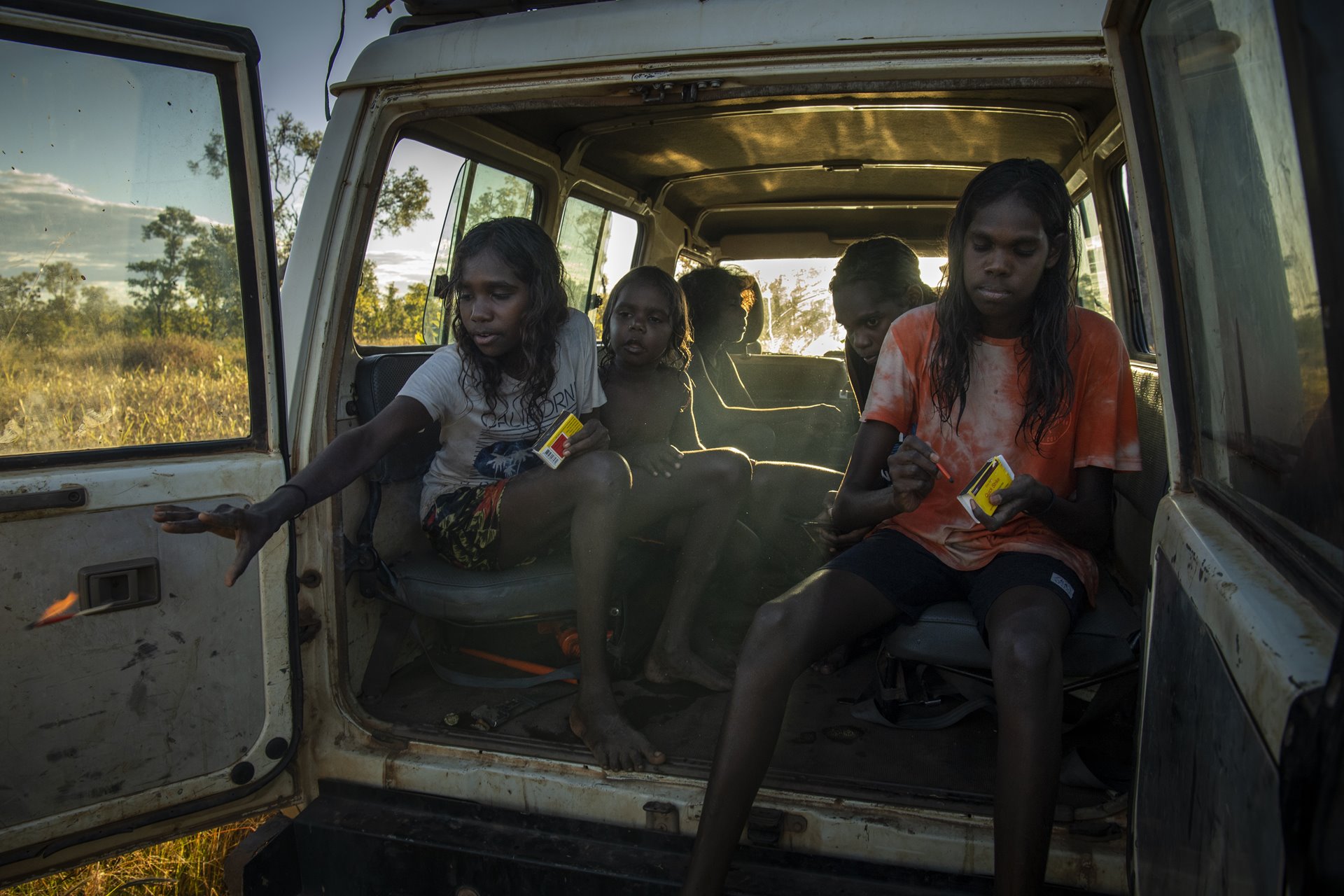 Young people throw specially designed matches from the back of a car, lighting small fires. Narwarddeken children are encouraged to carry out controlled burning by elders, as part of an education that teaches them to know the land and how to look after it.