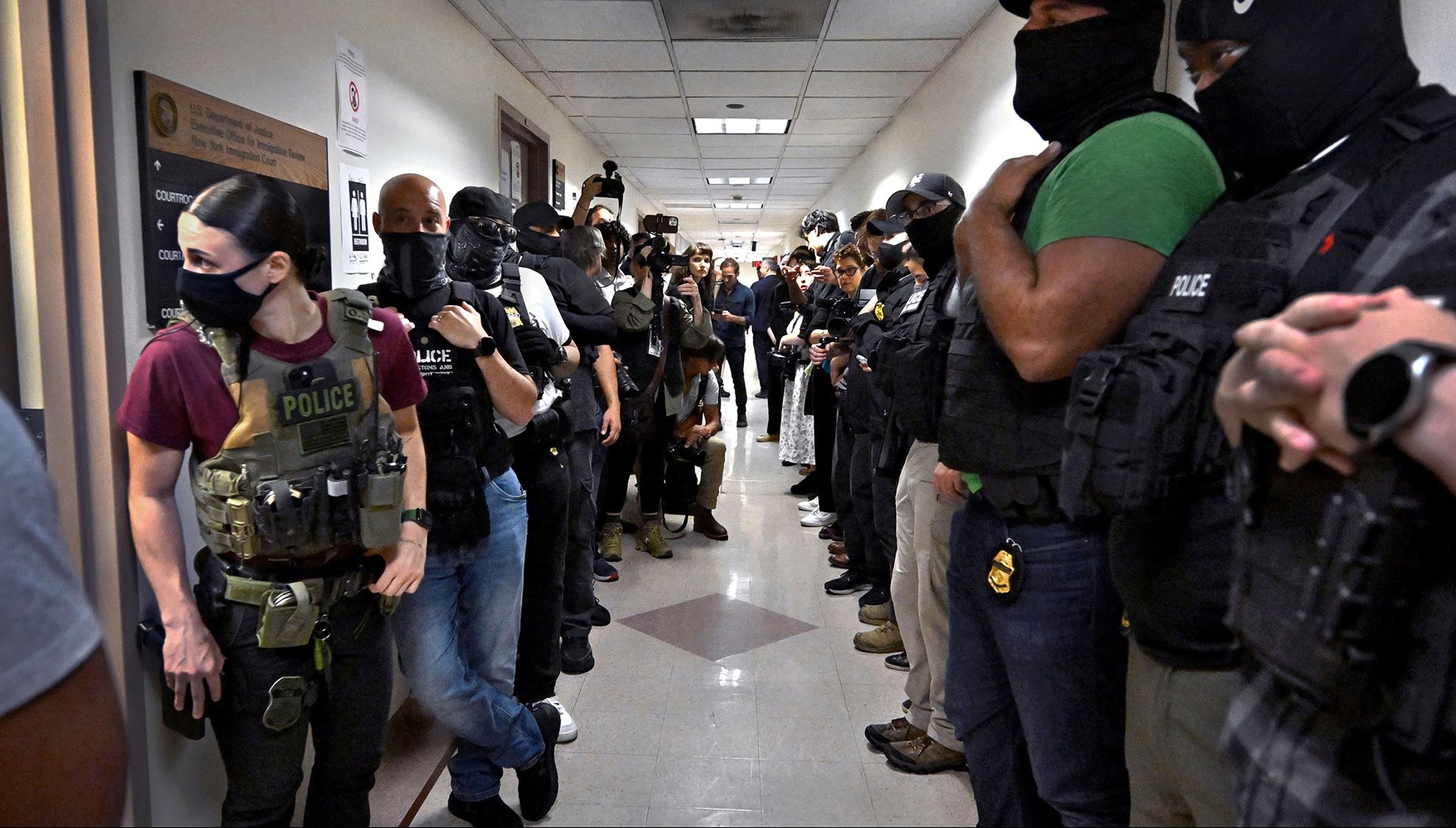 <p>Masked federal officers wait outside courtrooms holding target photographs. While ICE claims masks protect the identity of agents and their families, critics argue the practice erodes accountability and public trust.&nbsp;New York City, New York, United States&nbsp;</p>
