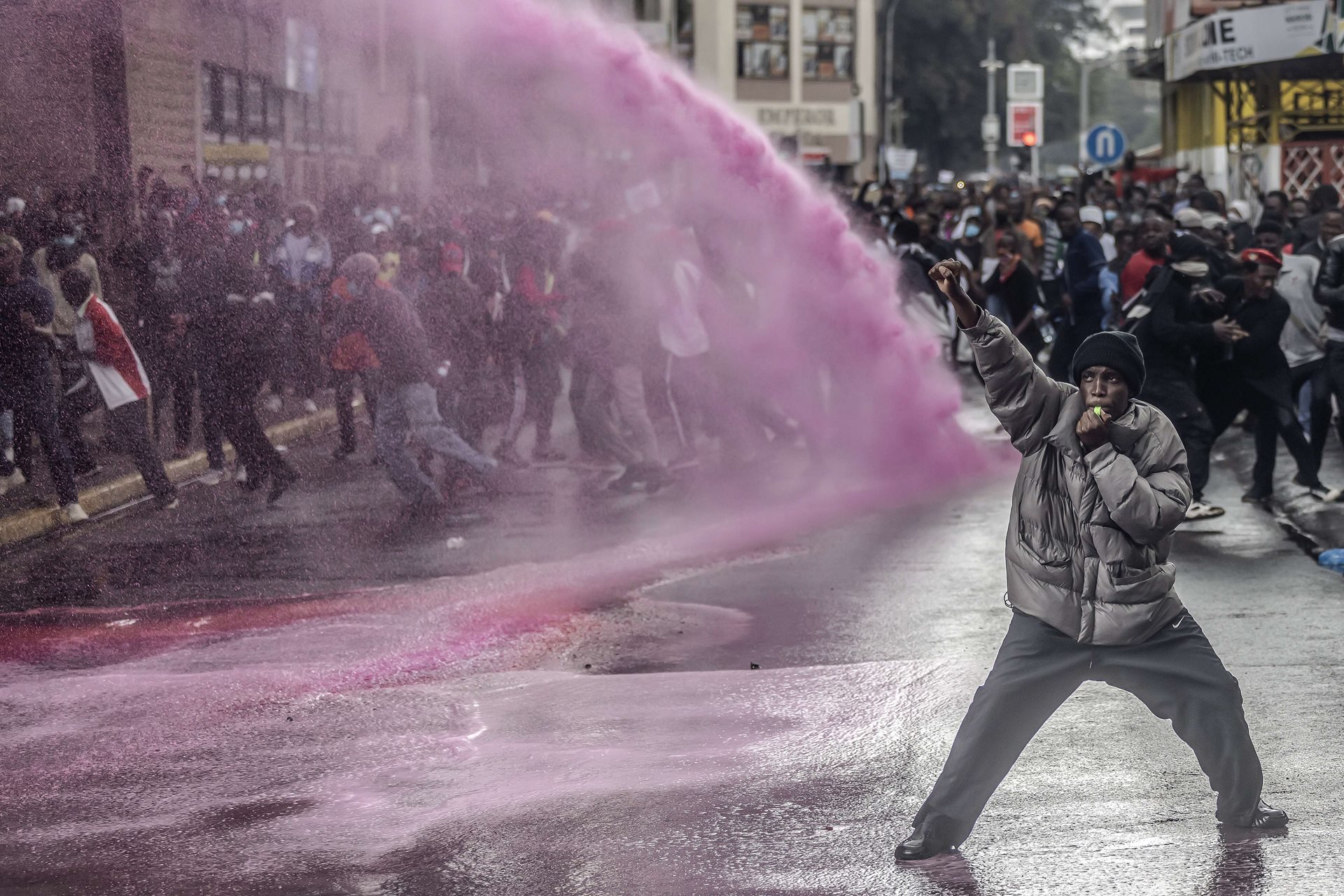 A protestor raises a fist in defiance as Kenyan police officers use a water cannon to disperse the gathering in Nairobi, Kenya. Pink dye in the water is often used by police at protests to mark individuals for identification.