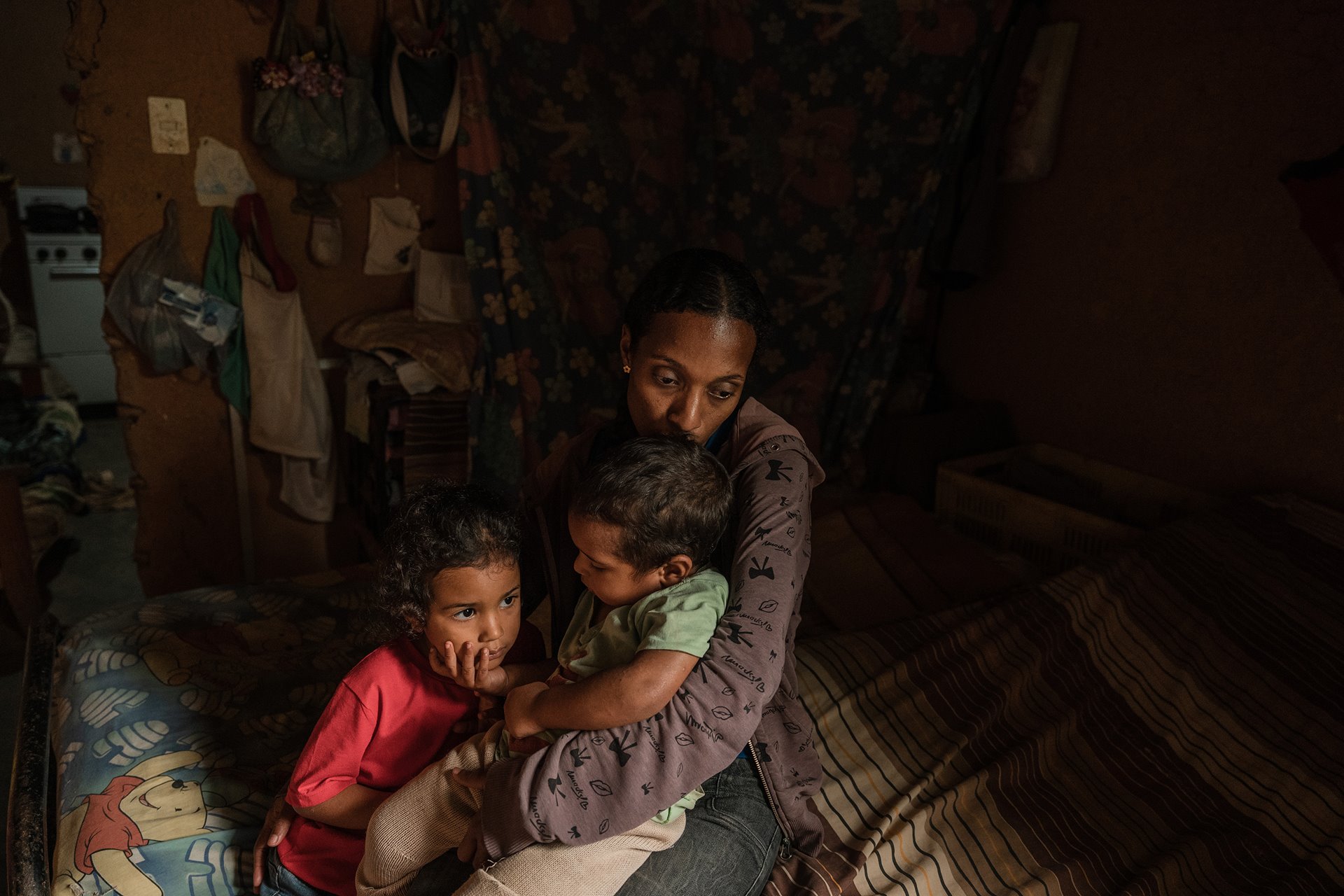 Yrelys Jimenez (38) holds her son Yonder Lopez-Jimenez (2) and her daughter, Clarelys Lopez-Jimenez (4) on the bed that the family shares, in San Diego de Los Altos, Venezuela. Her US$6 monthly salary barely covers her basic needs, so she plants beans and avocados to barter with her neighbors.
