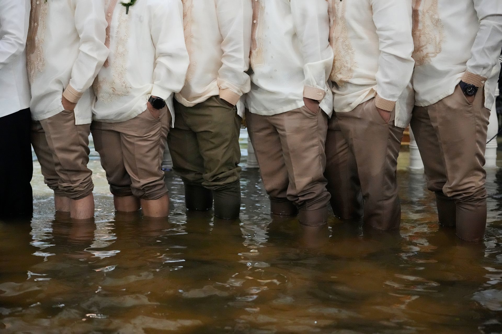 Groomsmen and guests wearing <em>barong tagalog</em>, the national dress of the Philippines, stand knee-deep in floodwaters. Local advocates increasingly link flooding to systemic failures in infrastructure and resource management. Malolos, Bulacan province, Philippines