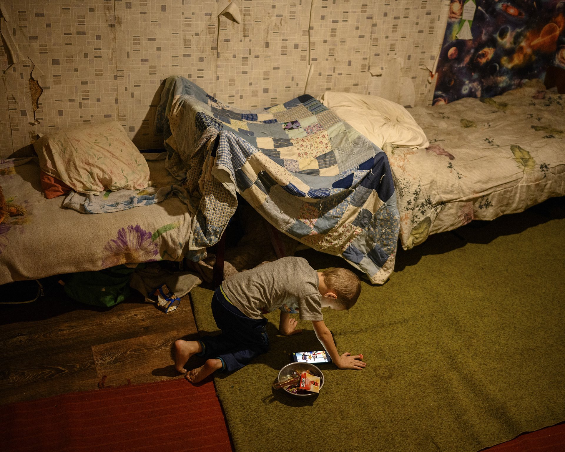 A boy plays a video game on a cell phone in his mother&rsquo;s bedroom in Zaitseve, Donbas, Ukraine, a few hundred meters from the &nbsp;front line of the conflict between Ukrainian and separatist forces. The village of Zaitseve is split in two &ndash; one part is controlled by separatists, the other by government forces.