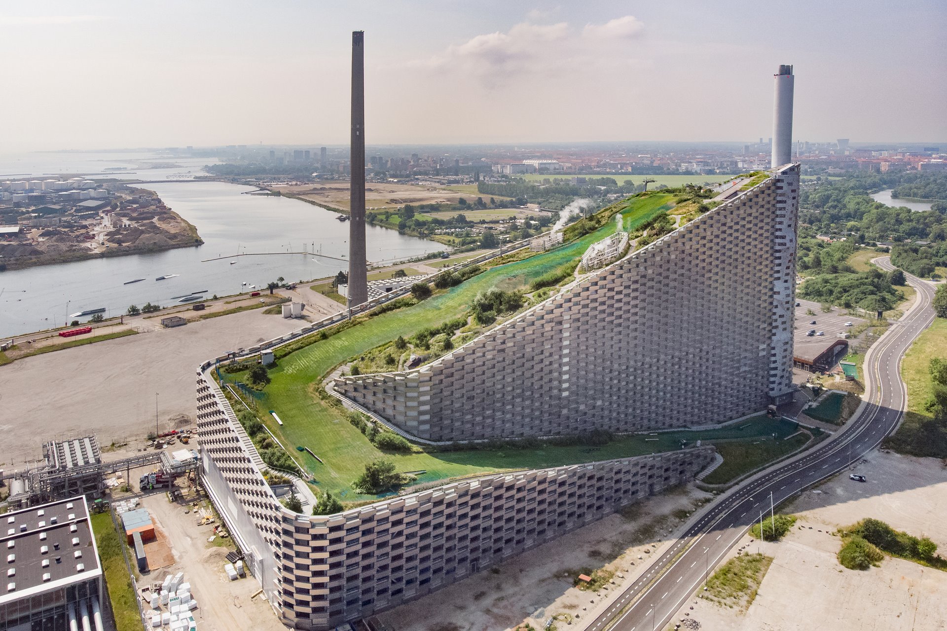 This waste-to-energy heat-and-power plant in the industrial outskirts of Copenhagen, Denmark, burns around 440,000 tons of waste a year to supply more than 30,000 homes in and around Copenhagen with electricity, and 72,000 homes with heating (recycled from flue gas condensation using heat pumps). The plant uses a filter to remove harmful pollutants from its incineration exhaust, and hosts an all-seasons ski run and public green space on its roof.